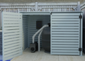 A gray aluminum pool pump cover with a lift-up lid and side door open, revealing a pool pump inside.