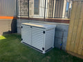 Outdoor storage unit against a wall with grass and wooden fence in the background